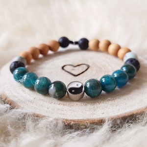 Könnte beinhalten: Ein blaues und grünes Edelstein-Armband mit einem silbernen Yin-Yang-Anhänger. Das Armband besteht aus Holzperlen, Lavasteinen und anderen Edelsteinen.