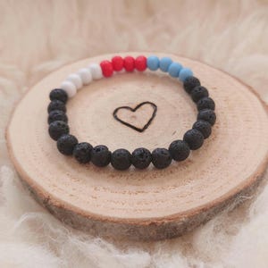 Puede incluir: Un brazalete de cuentas de roca volcánica negra con cuentas de acento blancas, rojas y azules.