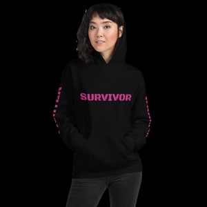 Puede incluir: Sudadera con capucha negra con un gráfico rosa "SURVIVOR" en la parte delantera y el texto rosa "SURVIVOR" repetido en las mangas.