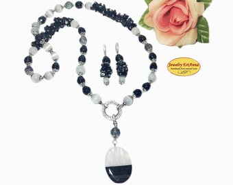 Puede incluir: Un collar de cuentas negras y blancas con un gran colgante ovalado y pendientes a juego. El collar presenta un anillo plateado con piedras transparentes y un colgante de ágata negro y blanco. Los pendientes están hechos de cuentas negras y plata.