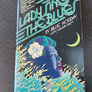 May include: A book cover with a blue and yellow illustration of a woman singing. The title of the book is "Lady Sings the Blues" by Billie Holiday with William Dufty. The book cover is black with white text.