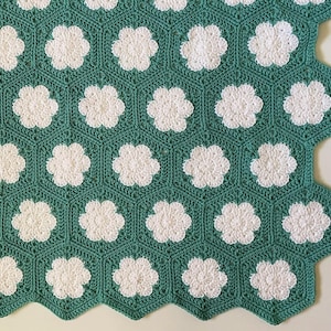 K&ouml;nnte beinhalten: Eine gr&uuml;ne H&auml;keldecke mit einem sechseckigen Muster mit wei&szlig;en Blumenmotiven.