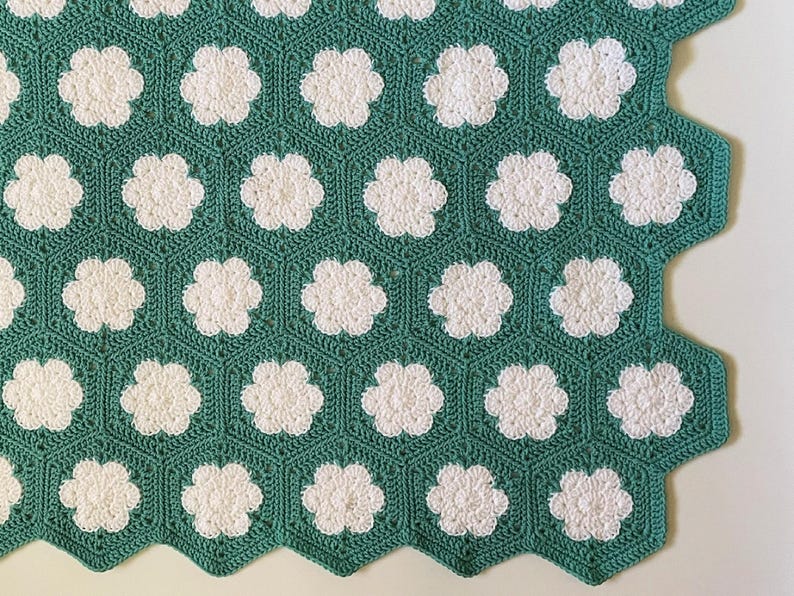 K&ouml;nnte beinhalten: Eine gr&uuml;ne H&auml;keldecke mit einem sechseckigen Muster mit wei&szlig;en Blumenmotiven.
