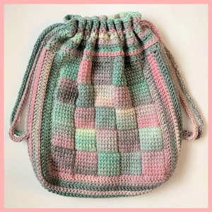 Peut inclure: Un sac à cordon en crochet avec un motif patchwork dans des tons de rose, vert et gris.