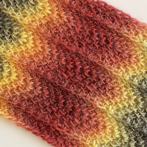May include: A close-up of a multi-colored knitted scarf with a textured pattern. The scarf is made of yarn in shades of green, yellow, orange, and red.