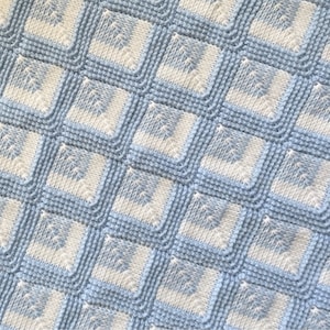 Puede incluir: Una manta de bebé de punto azul y blanco con un patrón cuadrado.