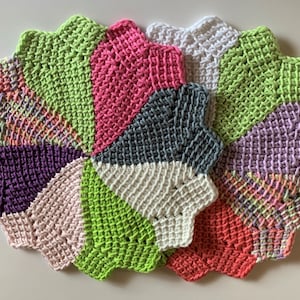 K&ouml;nnte beinhalten: Ein Set aus sechs geh&auml;kelten Untersetzern in verschiedenen Farben, darunter Rosa, Gr&uuml;n, Lila, Wei&szlig; und Grau. Die Untersetzer sind sternf&ouml;rmig und haben einen gewellten Rand.