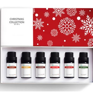 May include: A set of six 10ml essential oil bottles in a white box with a red lid. The bottles are labeled with the names of Christmas scents: Cinnamon, Nutmeg, Clove Bud, Candy Cane, Holiday Joy, and Pine Needle. The box has a red lid with a white snowflake pattern. The text "Christmas Collection Set of 6" is printed on the box.