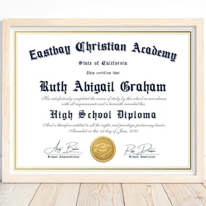 May include: A blue and gold high school diploma certificate with the name Ruth Abigail Graham printed in a decorative font. The certificate is framed in a light wood frame and has a gold seal with a graduation cap and a quill pen.