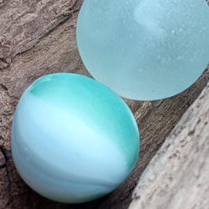 Odd opaque white and teal green Seaglass marble. This must have been a dudd due to one flat side. Such a unique piece of history