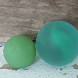Mini opaque green seaglass marble and green cats eye marble both perfectly frosted weathered and worn by the waves and turf of the ocean