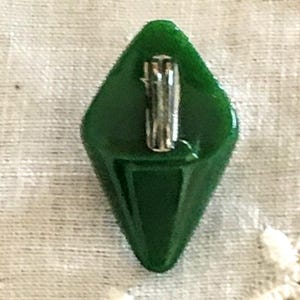 May include: A dark green glass button in the shape of a diamond with a silver pin on the back.