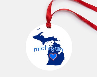 May include: A white round ornament featuring a blue outline of the state of Michigan and the word "michigan" in blue text. A blue heart with a red outline is in the centre of the state.