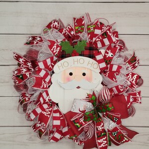 May include: A Christmas wreath with red and white striped ribbon, white mesh, and a Santa Claus face with the words "Ho, Ho, Ho" on it.