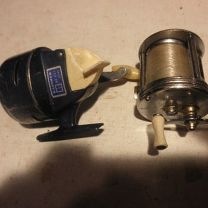 May include: Two vintage fishing reels. One is blue and white with the text "Eastman 145-00" on it. The other is silver with a white handle.