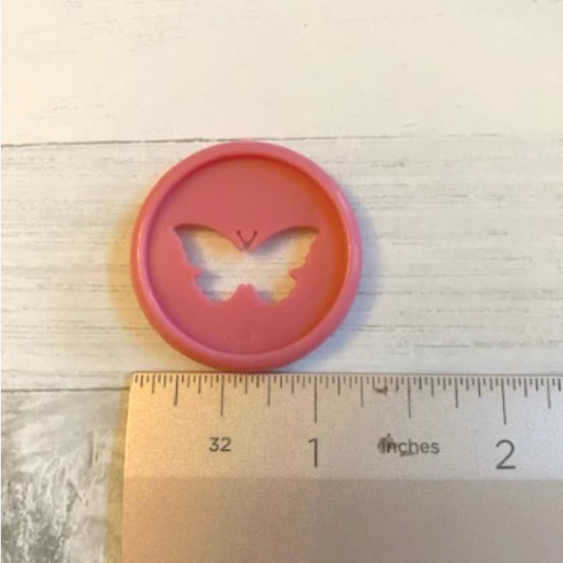 K&ouml;nnte beinhalten: Ein rosa-farbener, plastik-f&ouml;rmiger Ausstecher in Form eines Schmetterlings mit einem Durchmesser von etwa 2,5 cm.