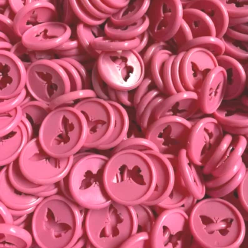 K&ouml;nnte beinhalten: Ein gro&szlig;er Haufen rosa Plastikkn&ouml;pfe mit einem Schmetterlingsdesign.