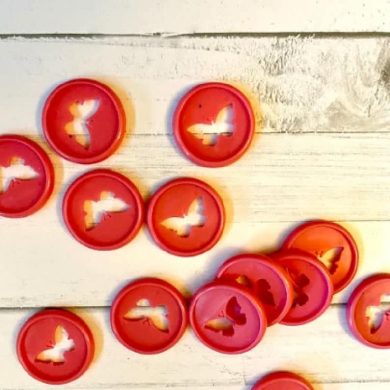 K&ouml;nnte beinhalten: Eine Sammlung roter, plastik-schmetterlingsf&ouml;rmiger Hefter. Die Hefter sind in einem Halbkreis auf einer wei&szlig;en Holzoberfl&auml;che angeordnet.