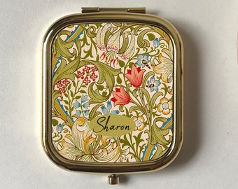 Op de afbeelding: Een gouden compact spiegel met een bloemenontwerp. De spiegel heeft een witte achtergrond met rode, gele, groene en blauwe bloemen. De naam "Sharon" is in goud op de spiegel gedrukt.