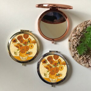 Peut inclure: Deux miroirs compacts ronds de couleur or avec une peinture de tournesols sur le devant. La peinture est une reproduction des "Tournesols" de Vincent van Gogh. Les miroirs ont une charni&egrave;re argent&eacute;e et un miroir en verre clair &agrave; l'int&eacute;rieur. Le nom "Sarah" est &eacute;crit sur le devant de chaque miroir.