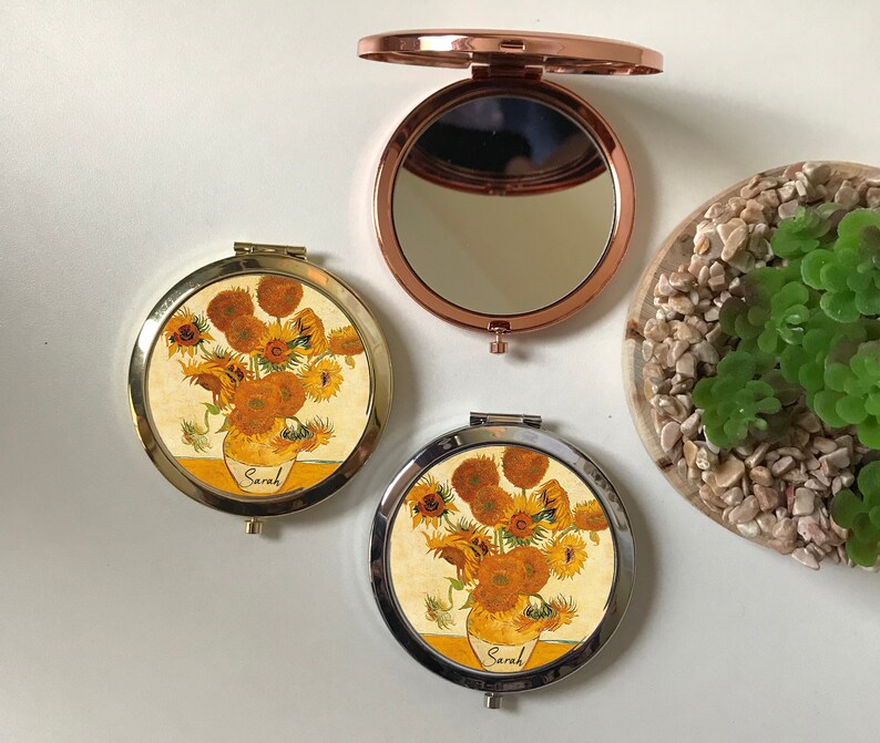 Peut inclure: Deux miroirs compacts ronds de couleur or avec une peinture de tournesols sur le devant. La peinture est une reproduction des "Tournesols" de Vincent van Gogh. Les miroirs ont une charni&egrave;re argent&eacute;e et un miroir en verre clair &agrave; l'int&eacute;rieur. Le nom "Sarah" est &eacute;crit sur le devant de chaque miroir.