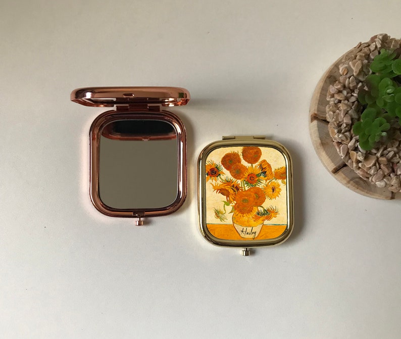 Peut inclure: Deux miroirs de poche, l'un avec une finition or rose et un miroir clair, l'autre avec une finition dor&eacute;e et une image imprim&eacute;e de tournesols dans un vase. L'image de tournesol est intitul&eacute;e "Van Gogh".