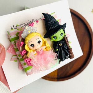 May include: A handmade polymer clay figurine set featuring a pink-dressed princess with a crown and a green witch wearing a black hat and holding a broom. The figurines are on a white card with the text "Homemade Amond".