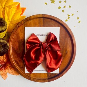 May include: A large, burgundy satin bow on a wooden surface. The bow is handmade and has a tag that says "homemadeamandasugar".