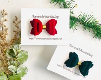 May include: Two velvet hair bows, one red and one green, with gold centers. The bows are displayed on white cards with the text "HomemadeAmandasWay" and a website address.