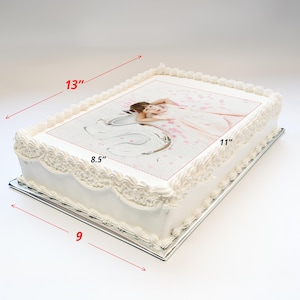 May include: A white cake with a photo of a girl in a white dress on top. The cake is 13 inches long, 11 inches wide, and 8.5 inches tall. The cake is on a silver cake board.