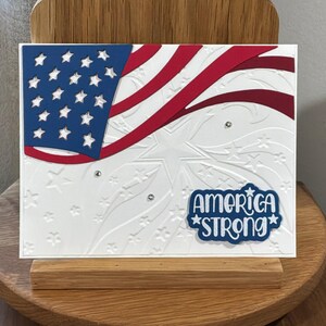 Tarjeta con la bandera estadounidense ondeando: estrellas en relieve, brillo de diamantes de imitación, "America Strong" (Estados Unidos fuerte).