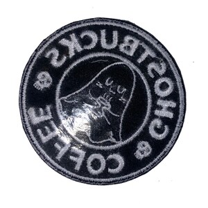Peut inclure: Un &eacute;cusson rond noir avec du texte brod&eacute; blanc et un motif de fant&ocirc;me. Le texte se lit "Coffee & Bucks Ghosts" sur le bord, avec un fant&ocirc;me au centre. Deux petits cr&acirc;nes sont &eacute;galement inclus dans le design.