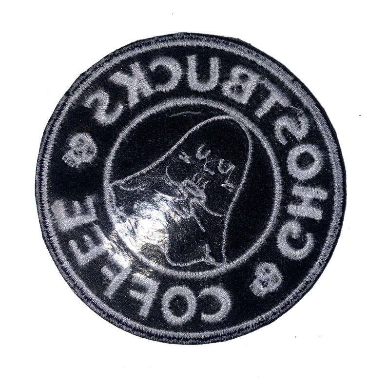 Peut inclure: Un &eacute;cusson rond noir avec du texte brod&eacute; blanc et un motif de fant&ocirc;me. Le texte se lit "Coffee & Bucks Ghosts" sur le bord, avec un fant&ocirc;me au centre. Deux petits cr&acirc;nes sont &eacute;galement inclus dans le design.
