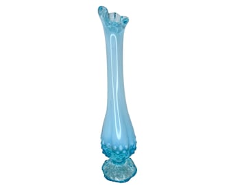 May include: A tall, light blue glass vase with a ruffled top and a textured, bulbous base. The vase has a slender, elongated body and is approximately 12 inches tall. The glass has a glossy finish, and the vase is set against a white background.