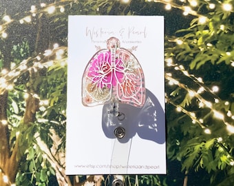 May include: A pink and white resin badge reel featuring a detailed anatomical illustration of human lungs with dried flowers and glitter embedded inside. The reel is attached to a white card with the text "Wisteria & Pearl" and "Personalized Accessories" printed on it. The text "www.etsy.com/shop/wisteriaandpearl" is printed at the bottom of the card.