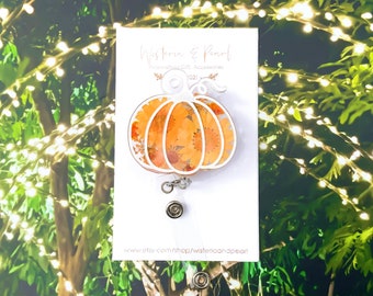 May include: White pumpkin-shaped retractable badge holder with a floral pattern. The badge holder is on a white card with the text "Wisteria & Pearl" and "Personalized Gift Accessories 2021".
