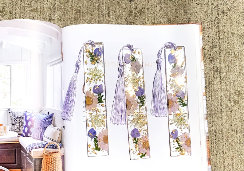 May include: Three purple and gold resin bookmarks with pressed flowers and a purple tassel.