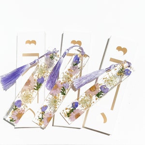 May include: Four purple and gold resin bookmarks with pressed flowers and a purple tassel.