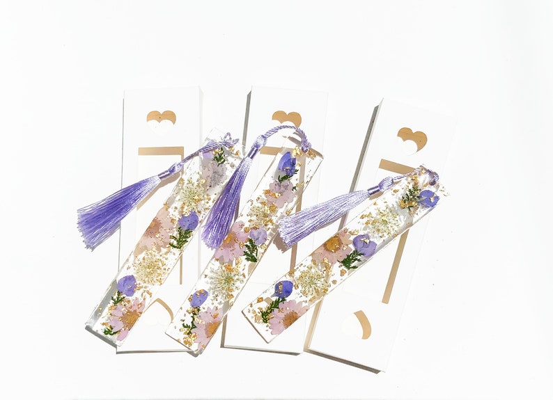 May include: Four purple and gold resin bookmarks with pressed flowers and a purple tassel.