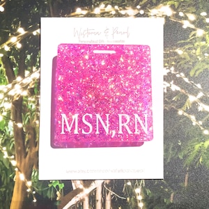 May include: A pink glitter badge holder with the text "MSN, RN" in white. The badge holder is rectangular with a hole at the top for a lanyard. The background is a white card with the words "Western & Pearl" at the top.