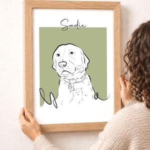 May include: A framed art print featuring a line drawing of a dog with the name "Sadie" above. The dog is white with black outlines, set against a muted green background. The frame is made of light-colored wood.