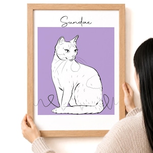 May include: A framed art print featuring a white cat illustration on a lavender background. The cat is drawn in a minimalist style with black outlines and a few spots. The word "Sundae" is written above the cat in cursive.