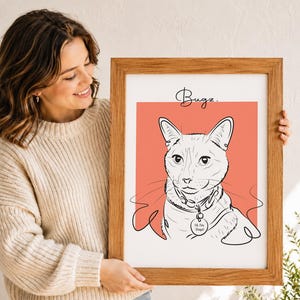 Puede incluir: Una l&aacute;mina de arte enmarcada con una ilustraci&oacute;n de l&iacute;nea negra de un gato sobre un fondo cuadrado color coral. El nombre Bugz est&aacute; escrito en cursiva sobre el gato, que lleva una placa en el collar con el texto Hi, I'm Bugz.