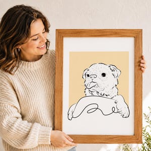 Puede incluir: Una l&aacute;mina art&iacute;stica enmarcada que presenta un dibujo de l&iacute;neas negras de un perro peque&ntilde;o con la lengua fuera, sobre un fondo amarillo claro s&oacute;lido. La ilustraci&oacute;n est&aacute; dentro de un marco rectangular de madera con acabado de veta natural.