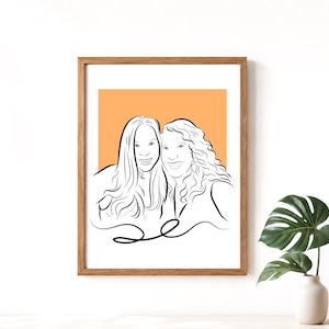 May include: A framed line art portrait of two smiling women with long hair. The artwork is in black lines against an orange background, set within a wooden frame. The portrait is displayed on a white surface.