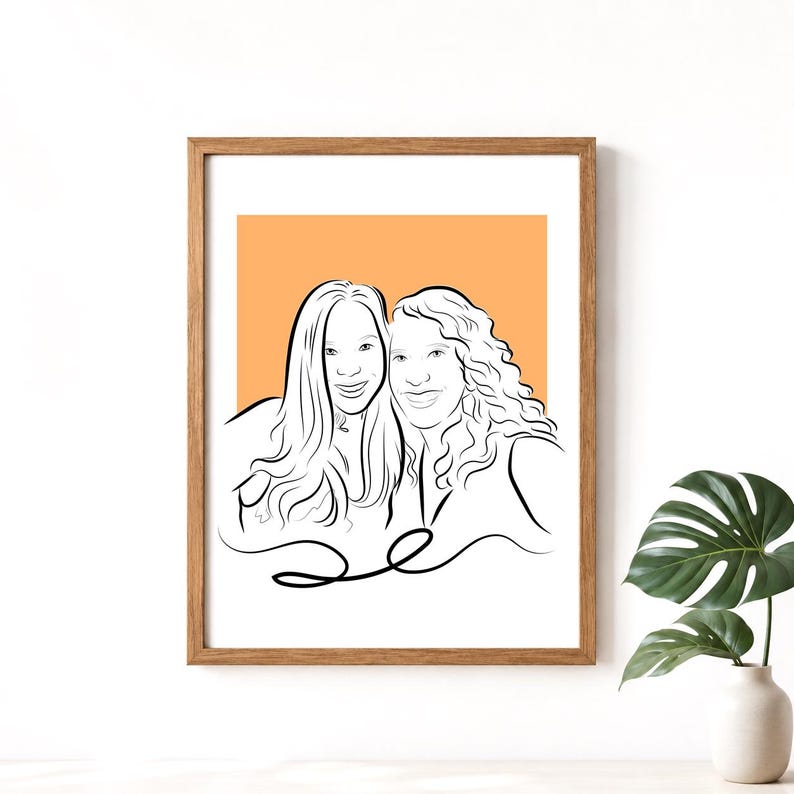 May include: A framed line art portrait of two smiling women with long hair. The artwork is in black lines against an orange background, set within a wooden frame. The portrait is displayed on a white surface.