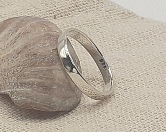 Op de afbeelding: Een eenvoudige zilveren bandring met een glad, afgerond oppervlak. De ring ligt op een lichtbruine stoffen achtergrond.