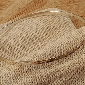 Puede incluir: Un brazalete de plata martillado. El brazalete es liso y brillante, con una textura martillada.