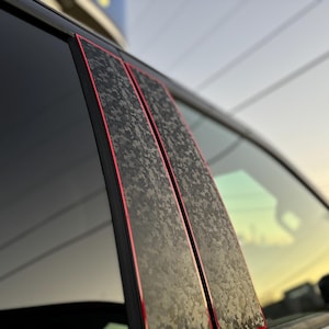 Könnte beinhalten: Nahaufnahme einer Autotür mit zwei schwarzen und grauen Tarnfolien mit roter Akzentlinie. Die Folien sind auf die Fensterverkleidung aufgebracht.