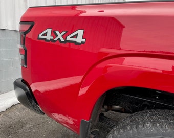 May include: A red pickup truck with a black 4x4 emblem on the side. The truck is parked in front of a white building.